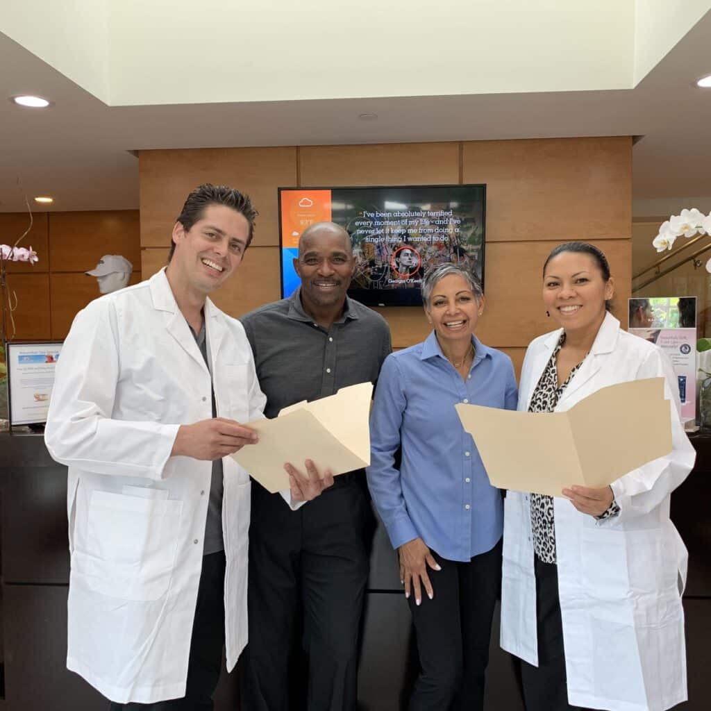 Nate Wilkins and Shebah Carfagna standing with two medical doctors in a modern clinic, smiling and holding folders, showcasing a positive and professional atmosphere.