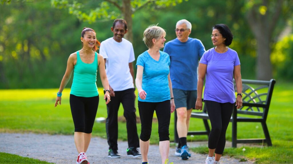 A diverse group of older adults walking together in a park, smiling and enjoying social connections while staying active.