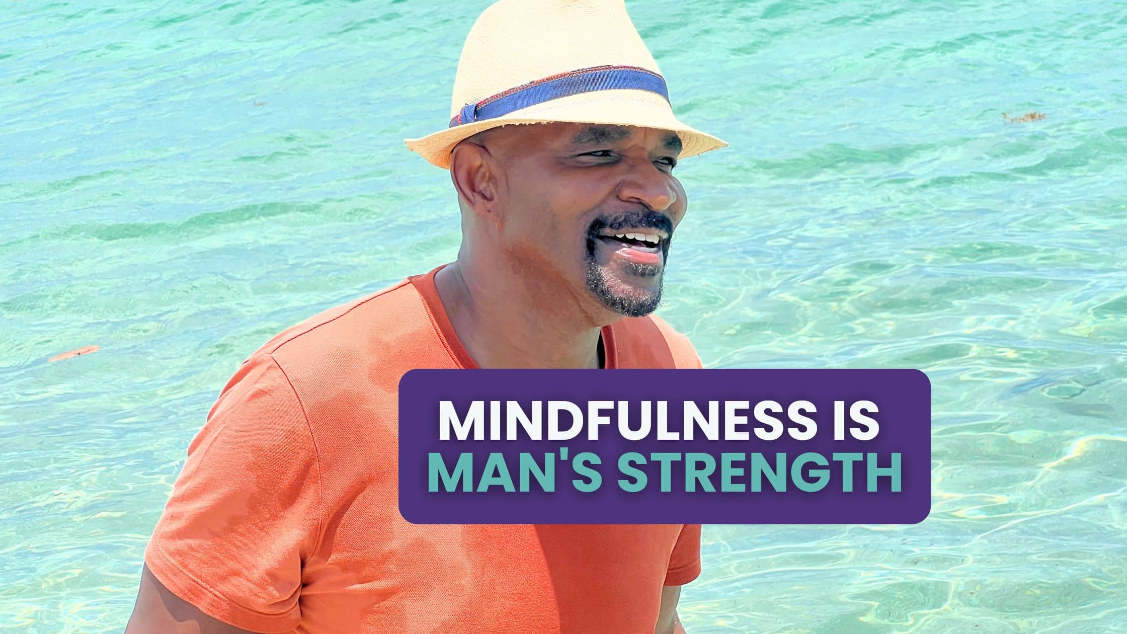 Smiling middle-aged Black man wearing a straw hat and orange shirt, standing in clear turquoise water, radiating joy and calm. (Nate Wilkins)