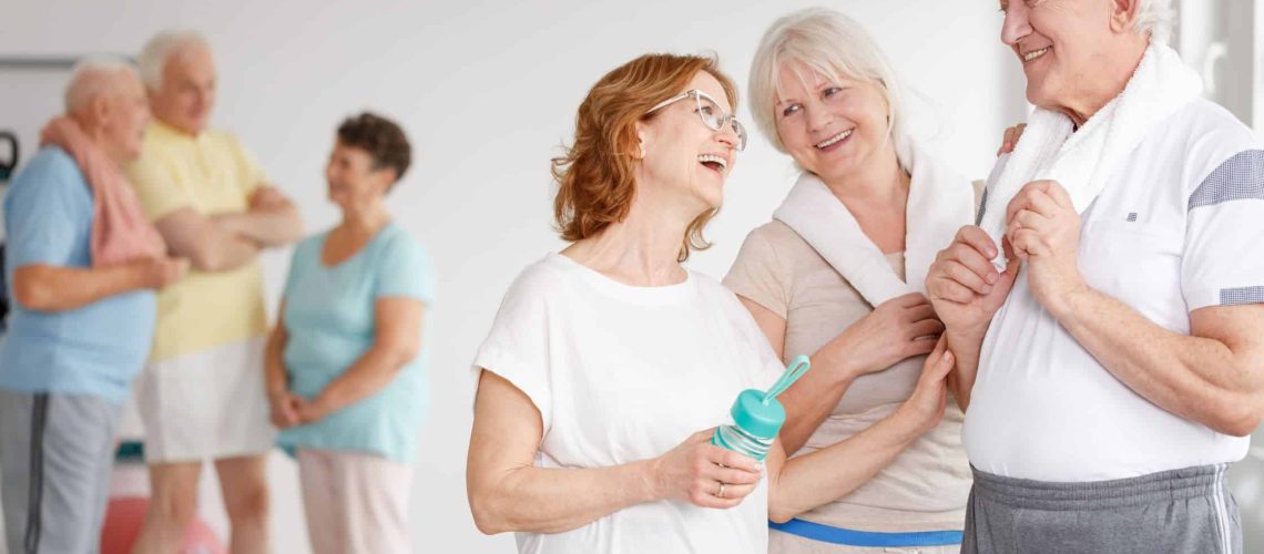 A group of happy seniors chatting and laughing after a fitness class, symbolizing the health benefits of staying socially connected.
